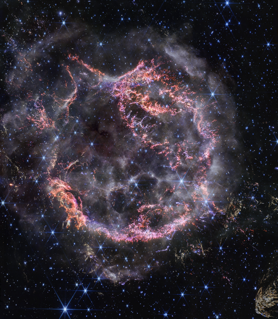 Vor einem dunklen Sternenhimmel mit vielen bläulich leuchtenden Sternen ist eine ringförmige Wolke zu erkennen. Einige Bereiche sind rötlich und knotig, andere sind weißlich und rauchähnlich.