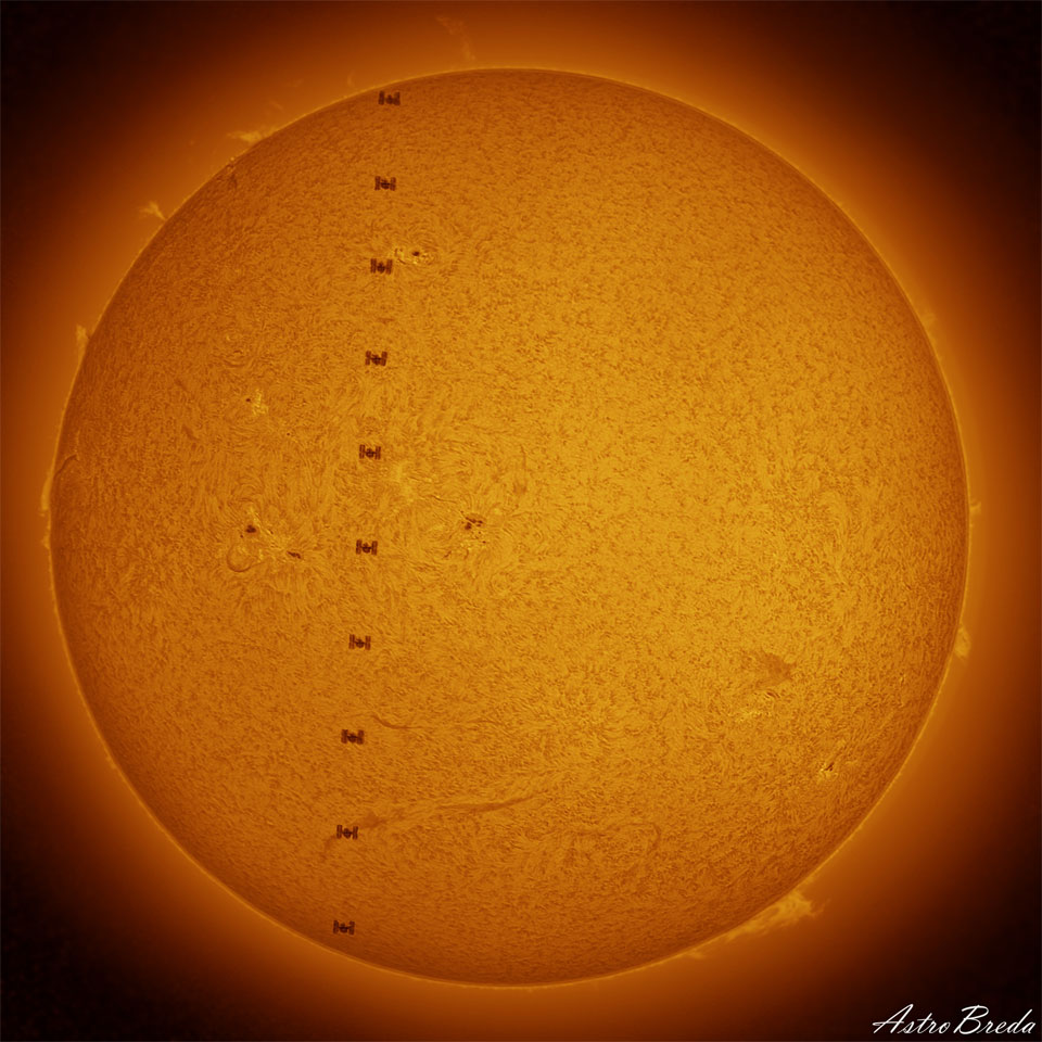 Vor der orangefarben leuchtenden Sonne zieht die Internationale Raumstation ISS vorbei. Die Sonne ist von Spikulen überzogen. Am Rand treten einige Protuberanzen auf.